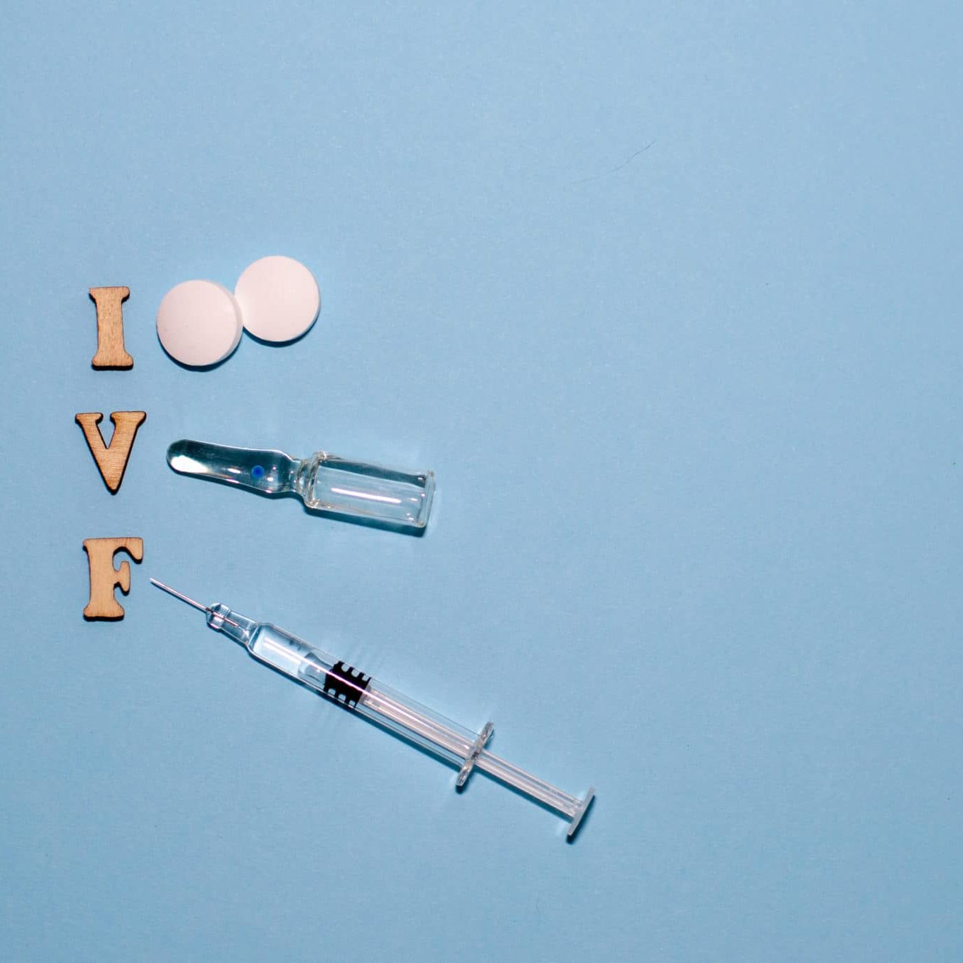 The Abbreviation IVF Is Laid Out In Wooden Letters On A Blue Background. In Vitro Injection Pen, Tablet And Ampoule. A Syringe With A Thin Huge. IVF Concept. Medication With Hormones. Infertility. Donor Options