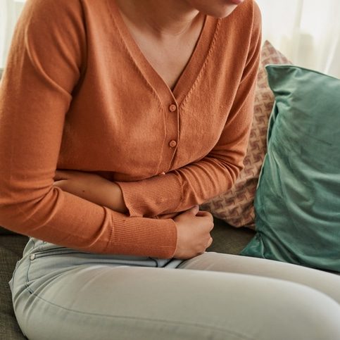 Shot Of A Woman Experiencing Stomach Pain While Lying On The Sofa At Home I need a heat pad, stat